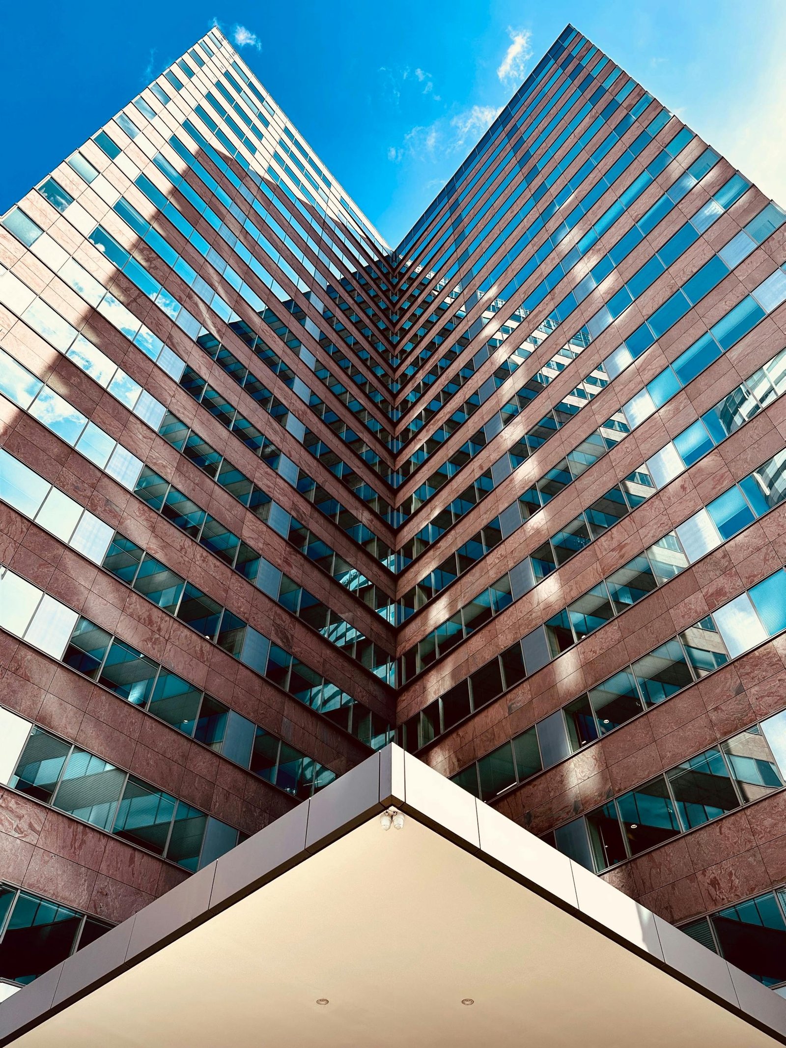 Upward view of a modern skyscraper with symmetrical lines and blue sky reflection.
